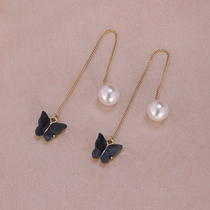 Close-up of gold chain earrings featuring black butterfly charms and white pearls