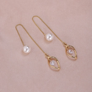 Macro detail of golden pearl drop earrings with hollow leaf charms on silk background
