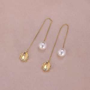 Detail view of gold chain earrings with smooth white pearls and yellow faceted gemstones