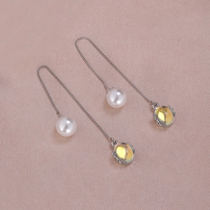 Detail of silver chain earrings featuring white pearls and yellow faceted gemstones on silk