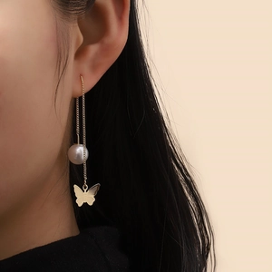 Elegant gold drop earrings with pearl and butterfly pendant worn by a model