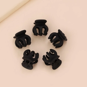 Cinq mini pinces à cheveux noires mates pour frange sur un fond rose doux