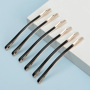 Set of six minimalist black and gold metallic hair pins displayed on a white marble stand