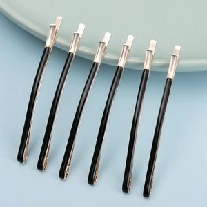 Set of six minimalist black and gold hair clips arranged neatly on a pastel background
