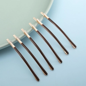 Detail of six minimalist dark coffee metal hair clips arranged on a ceramic dish