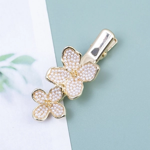 Détail de la pince à cheveux dorée avec deux fleurs élégantes en perles blanches