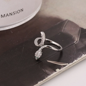 Elegant silver snake ring with sparkling white and green zircon stones on dark paper