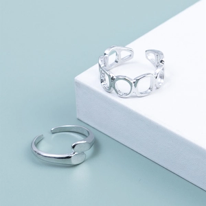 Close-up of geometric hollow chain and crisscross silver rings on a minimal display