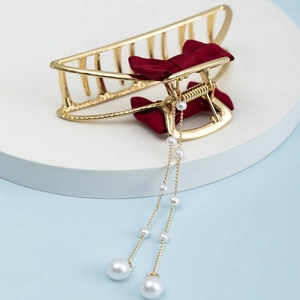 Detail view of a gold alloy shark clip with burgundy mesh bow and long pearl tassels