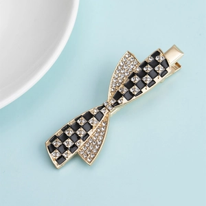 Close-up of golden bow-shaped hair clip with black and clear rhinestone checkerboard pattern