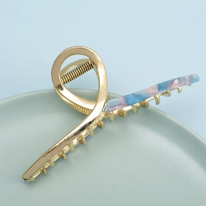 Golden metal hair claw clip with colorful marble acetate inlay in a ceramic tray