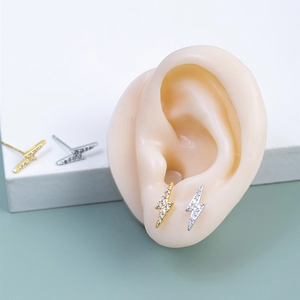 Détail de boucles d'oreilles éclair avec zircons sur un modèle d'oreille en silicone