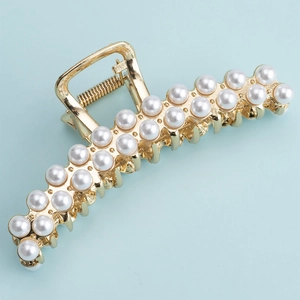 Detail of large gold metal shark clip with rows of white pearls on light blue surface