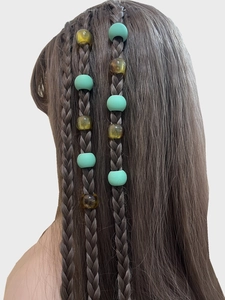 Close-up of matte mint green and amber resin beads on dark brown braided hair