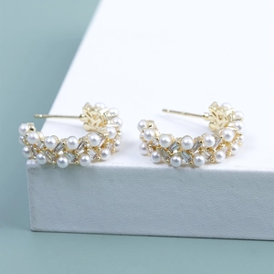 Detail of C-shaped gold earrings with embedded pearls and zircon stones on a green background