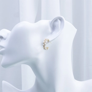 Detailed view of C-shaped gold earring with white pearls and sparkling zircons