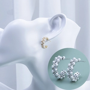 Elegant C-shaped earrings with pearls and baguette-cut zircons on a white display