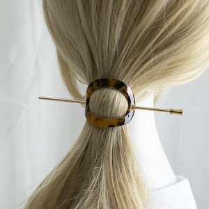 Detailed view of acetate tortoiseshell oval ring and gold metal hair pin in use