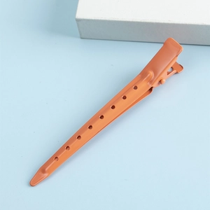 Pince à cheveux minimaliste en métal orange mat avec détails ajourés sur fond bleu ciel