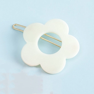 Barrette à cheveux fleur en résine blanc crème avec épingle dorée sur fond bleu