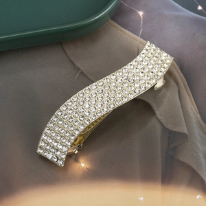 Détail de la barrette dorée courbée ornée de strass étincelants en pavé dense