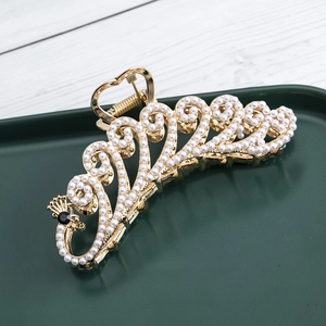 Golden peacock hair claw clip with white pearls and heart handle on a green tray