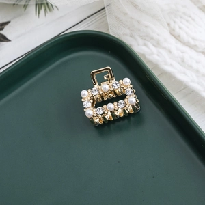 Mini pince à cheveux élégante en métal doré avec perles et strass sur plateau vert