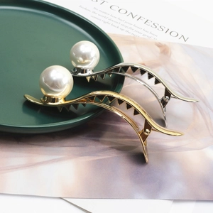 Close-up of elegant gold and silver metal hair clips with large white pearls on a tray