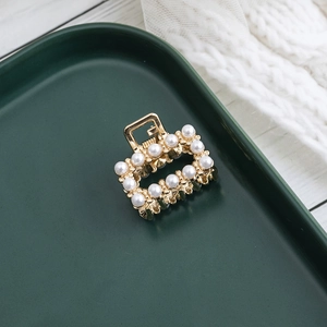 Détail d'une pince à cheveux en métal doré avec perles blanches sur un plateau vert chic