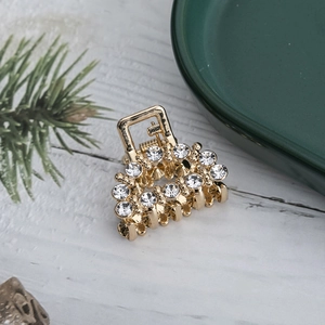 Detailed close-up of small golden hair claw with sparkling rhinestones on white wood