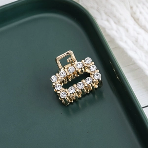 Détail d'une petite pince à cheveux dorée avec strass blancs et design rectangulaire évidé