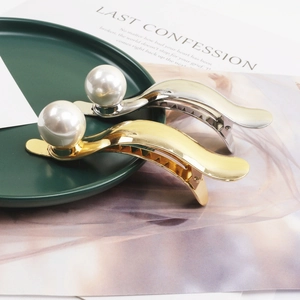 Elegant gold and silver metal hair clips with large pearls displayed on a decorative plate