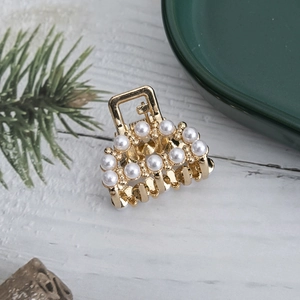 Detail of small gold hair claw with double rows of pearls on light wood background