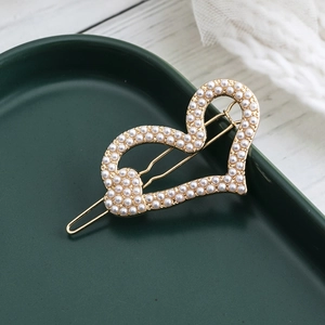Elegante gouden hartvormige haarspeld met parels op een groen keramisch dienblad