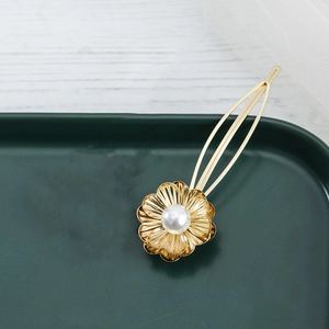 Eleganter goldener Blumen-Haarclip mit weißer Perle auf einer Vintage-Keramikschale