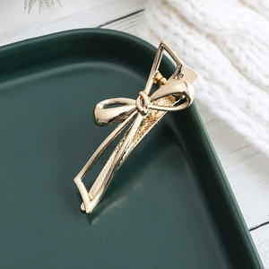 Eleganter goldener Schleifen-Haarclip mit polierter Oberfläche auf Keramiktablett