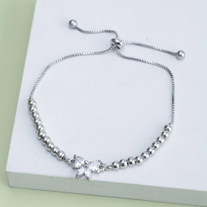 Detail of silver bow bracelet with zircons on stone display with green background