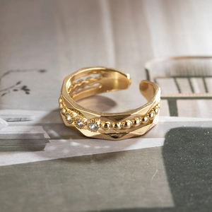 Detailed close-up of wavy gold ring with textured beads and four clear zircon stones