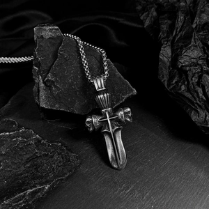 Detail of vintage silver titanium steel cross skull sword pendant on a dark rock background