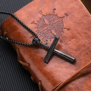Detailansicht einer mattschwarzen Kreuzkette auf Vintage-Leder mit Kompass-Prägung