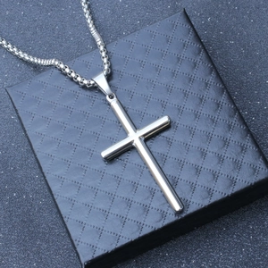Close-up of a polished stainless steel cross necklace on a luxury black jewelry box