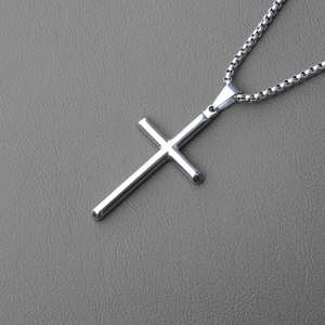 Macro shot of a silver steel cross pendant with a classic box chain on grey leather