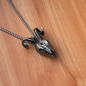 Detail of vintage ram skull pendant with oxidized finish on rustic wood background