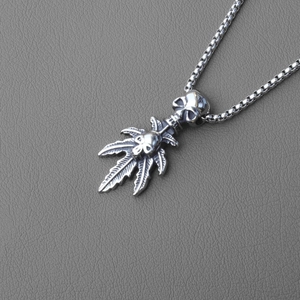 Macro detail of punk gothic necklace featuring skull charms and maple leaf pendant