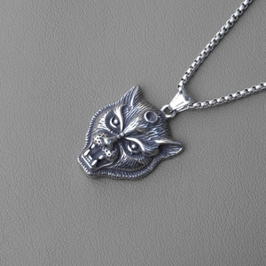 Macro shot of punk style wolf head pendant in vintage silver on a grey leather surface