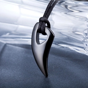 Macro shot of polished black wolf tooth pendant with woven cord on a dark display base