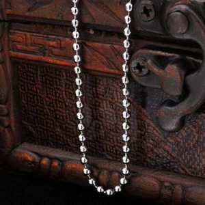 Polished silver beaded necklace chain displayed on vintage wooden jewelry box background
