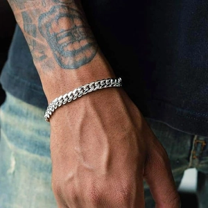 Close-up of a silver stainless steel Cuban link chain worn on a tattooed wrist
