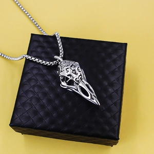 Silver vintage Viking raven skull necklace with engraved details on black box and yellow backdrop