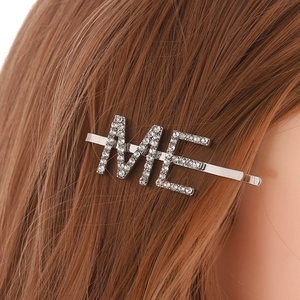 Gros plan d'une barrette argentée avec lettres ME en strass sur cheveux bruns